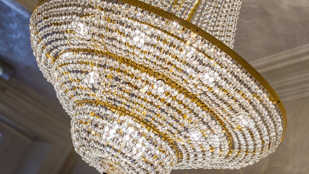 A chandelier with multiple tiers of clear crystal and gold accents. - The New Brooklyn (Blackpool)