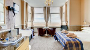 A hotel room with a bed, a desk, two chairs, a chandelier, and a large window with a view. - The New Brooklyn (Blackpool)