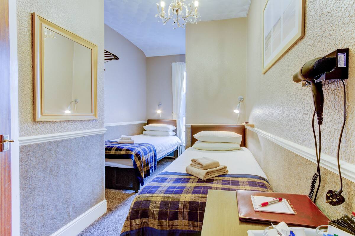 A hotel room with two beds, a mirror, a chandelier, a hairdryer, and a desk with a notebook and pen.