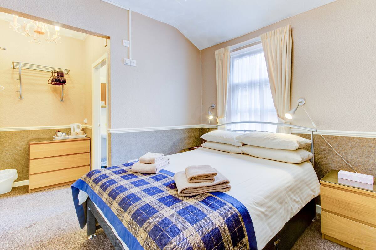 A hotel room with a bed, bedside table, nightstand, and a mirror.