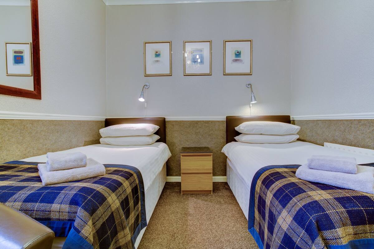 A hotel room with two beds, a nightstand, and a wall-mounted lamp.