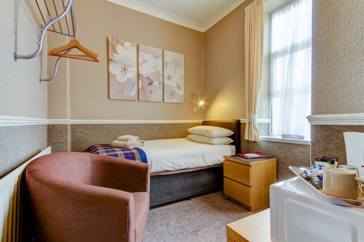 A hotel room with a bed, bedside table, chair, and a radiator.