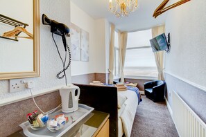 A hotel room with a bed, a desk with a kettle, a hairdryer, and a TV mounted on the wall. - The New Brooklyn (Blackpool)
