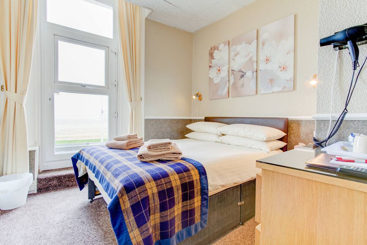 A hotel room with a bed, a desk with a hairdryer, and a window with curtains.