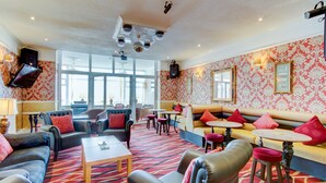 A spacious lounge area with multiple seating options including sofas and chairs, a coffee table, and a bar area with stools. - The New Brooklyn (Blackpool)