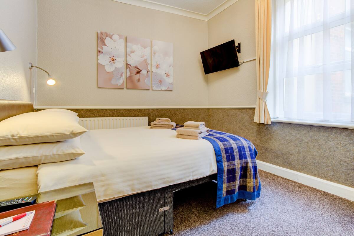 A neatly made bed with pillows, a blue plaid blanket, and folded towels on a headboard.