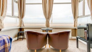 A room with a view of the beach, two brown chairs, a small round table, and a television on a stand. - The New Brooklyn (Blackpool)