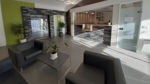 A modern lobby with a glass partition, seating area, and a reception desk. - L'Espace Thermal (Dax)