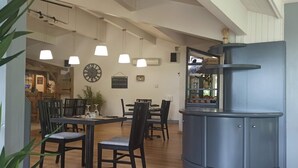 A dining area with wooden tables and chairs, pendant lights, and a clock on the wall. - L'Espace Thermal (Dax)