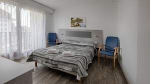 A modern hotel room with a large bed, two blue chairs, a wooden floor, and a painting on the wall. - L'Espace Thermal (Dax)