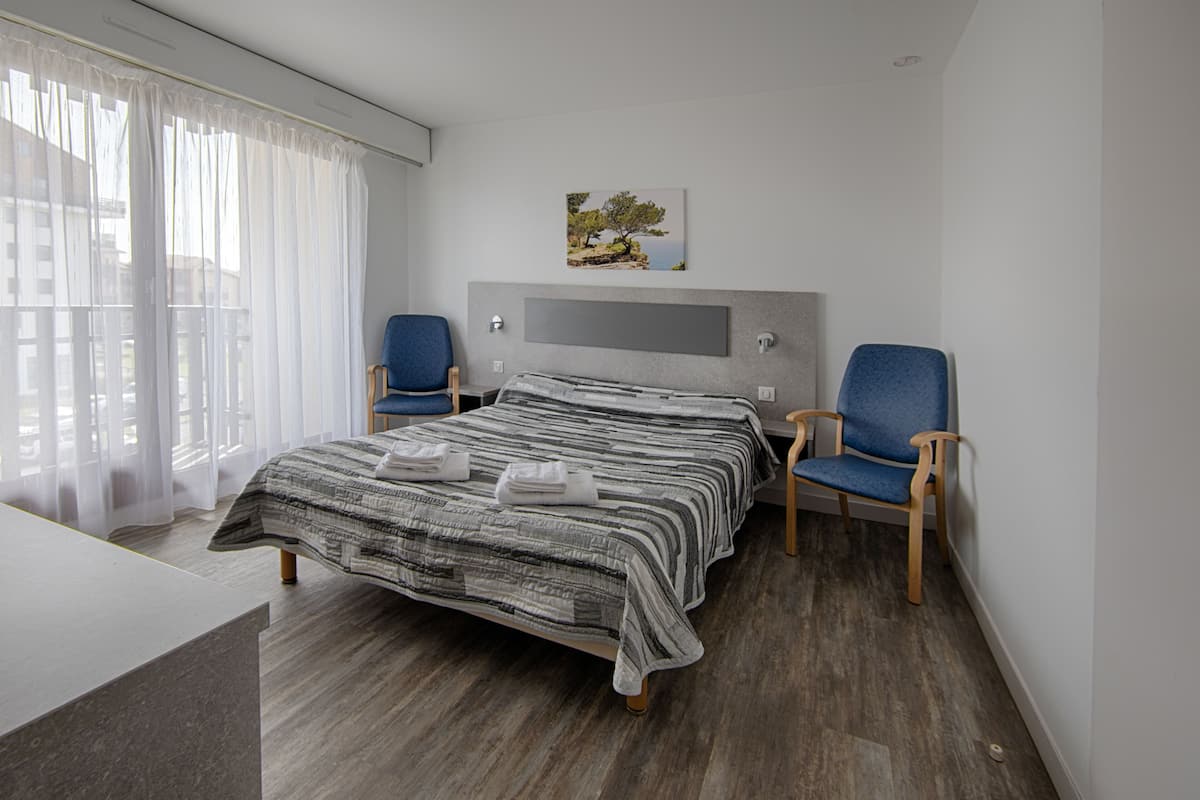 Ein modernes Hotelzimmer mit einem großen Bett, zwei blauen Stühlen, einem Holzboden und einem Bild an der Wand.