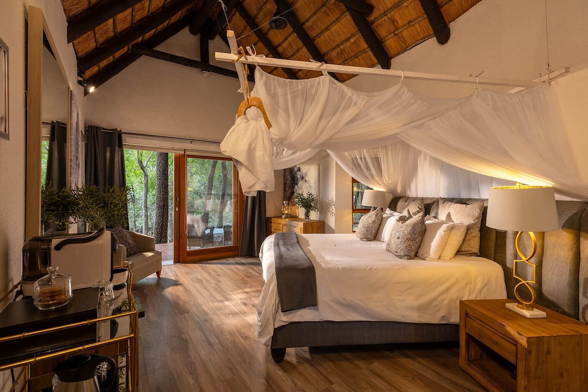 A bedroom with a canopy bed, a wooden desk with a coffee machine, and a view of the outdoors.