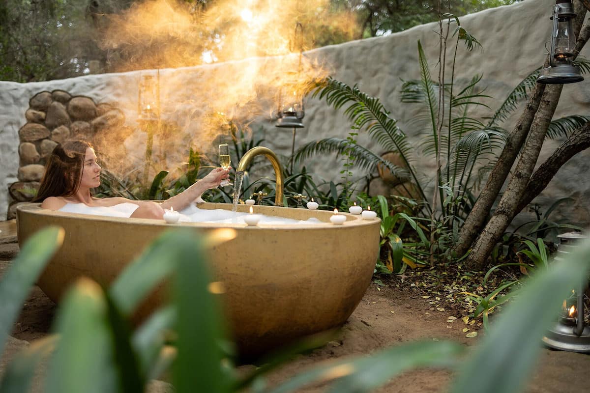 A woman relaxing in a hot tub with candles and a fire in the background.