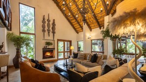A cozy living room with a fireplace, comfortable seating, and large windows offering a view of the outdoors. - Karongwe - Kuname Safari Lodge (Hoedspruit)