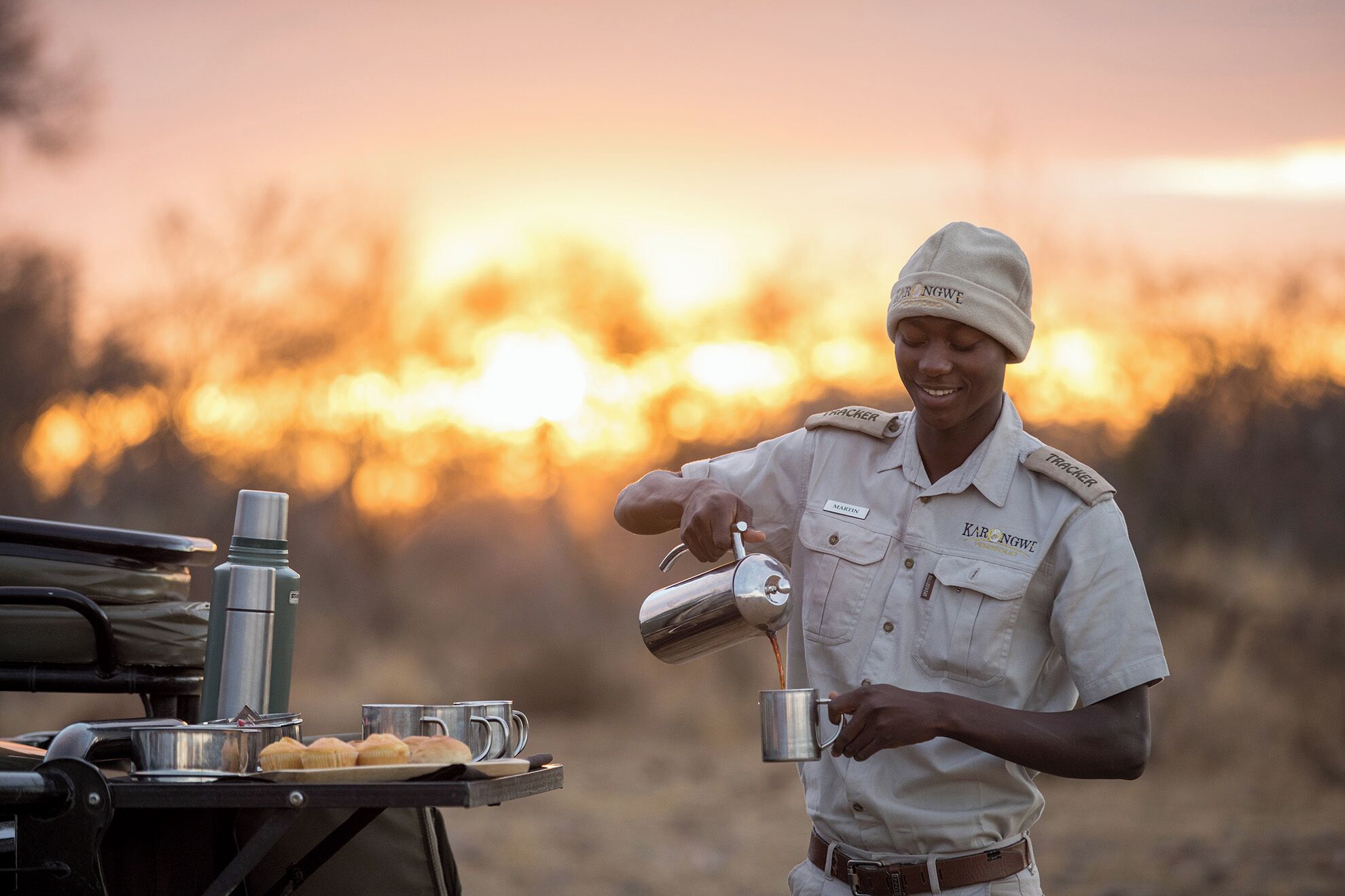 A person in a uniform pouring a beverage into a mug.