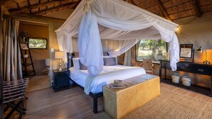A four-poster canopy bed with a wooden bench, bedside tables, and a desk with a lamp. - Karongwe - Chisomo Safari Camp (Tzaneen)