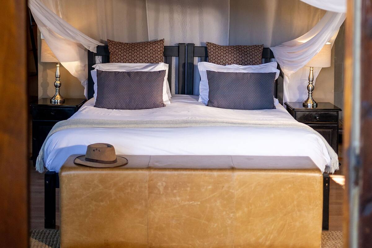 A bedroom with a canopy bed, a nightstand with a lamp, and a wooden ceiling.