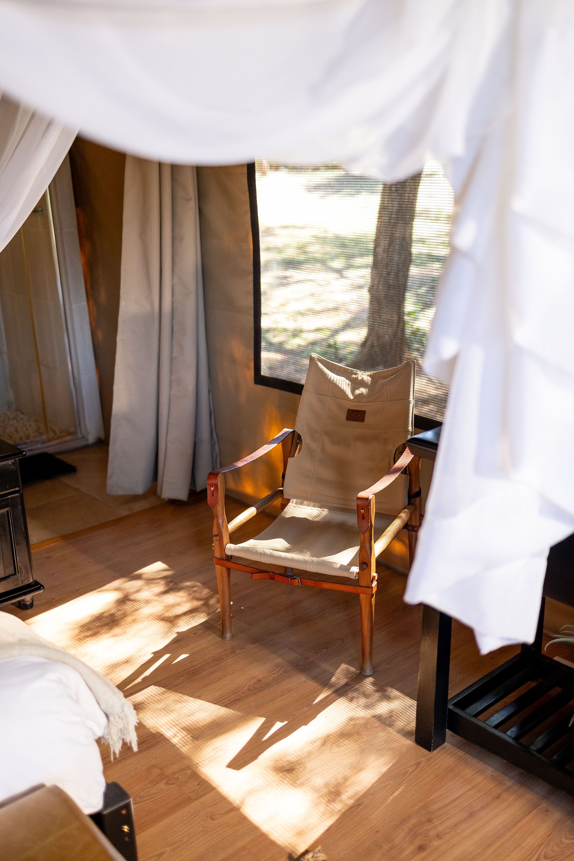 Un suelo de madera, una silla, un ventanal y cortinas.