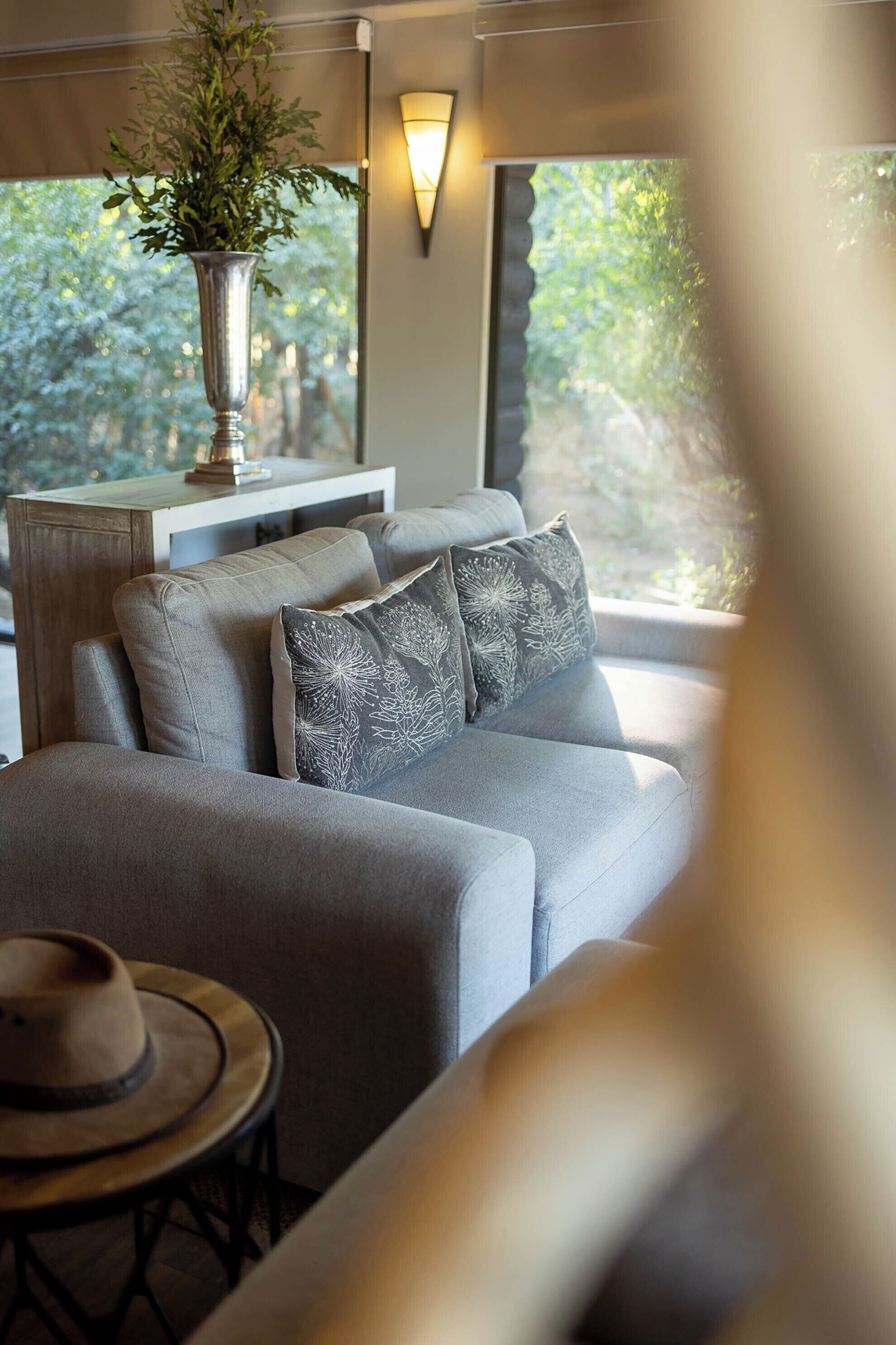 A modern living room with a sofa, decorative pillows, a vase with greenery, and a table with a hat.