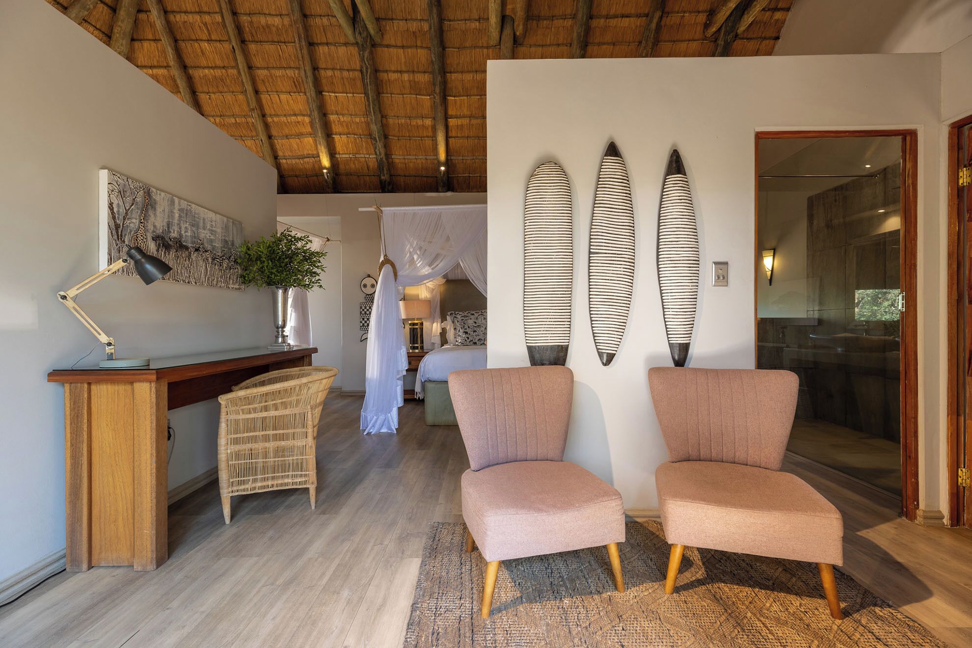 A room with a wooden desk, two chairs, a large plant, and a bed with a canopy.