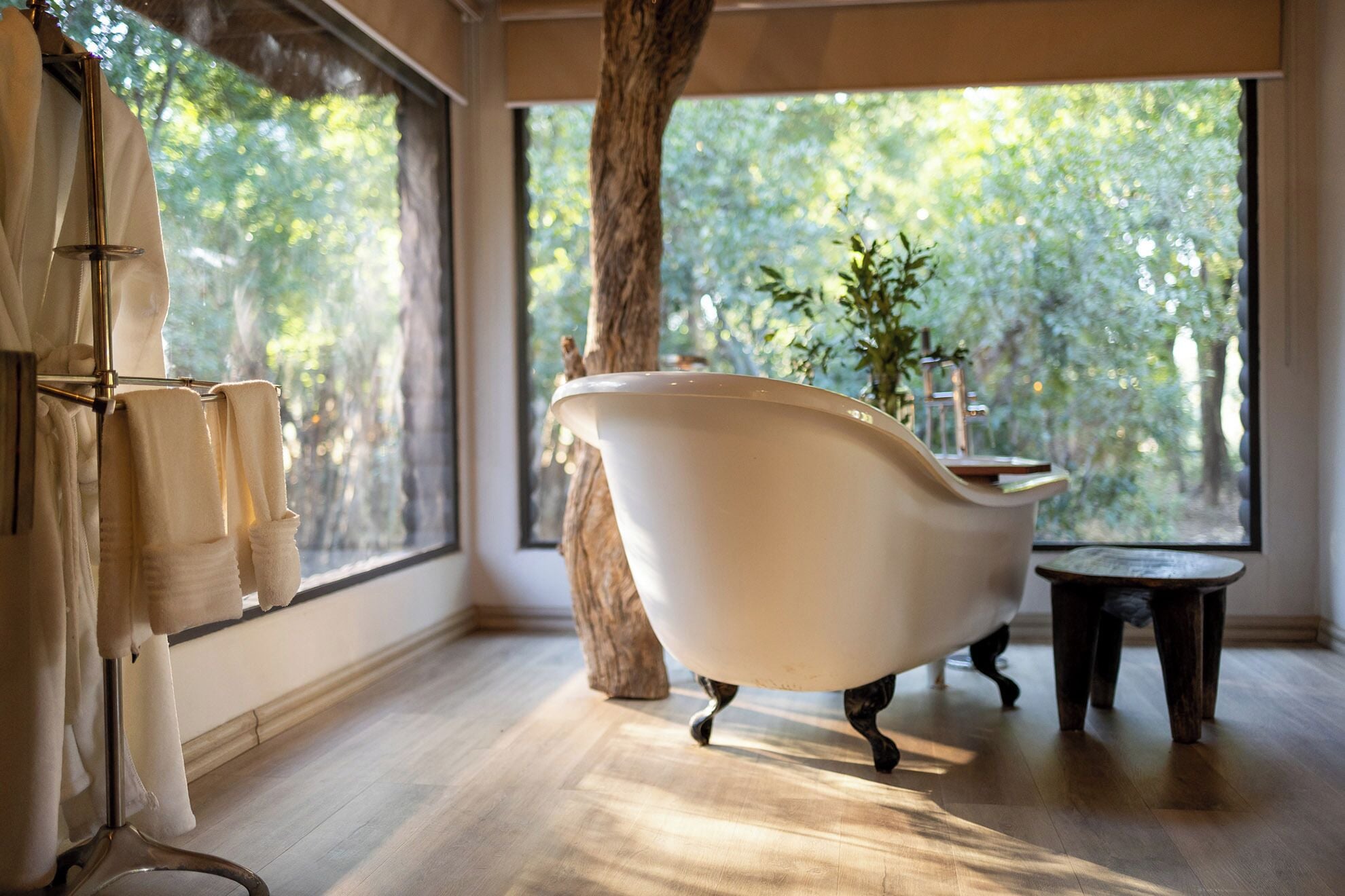 A bathroom with a freestanding bathtub, a wooden floor, and a large window with a view of trees.