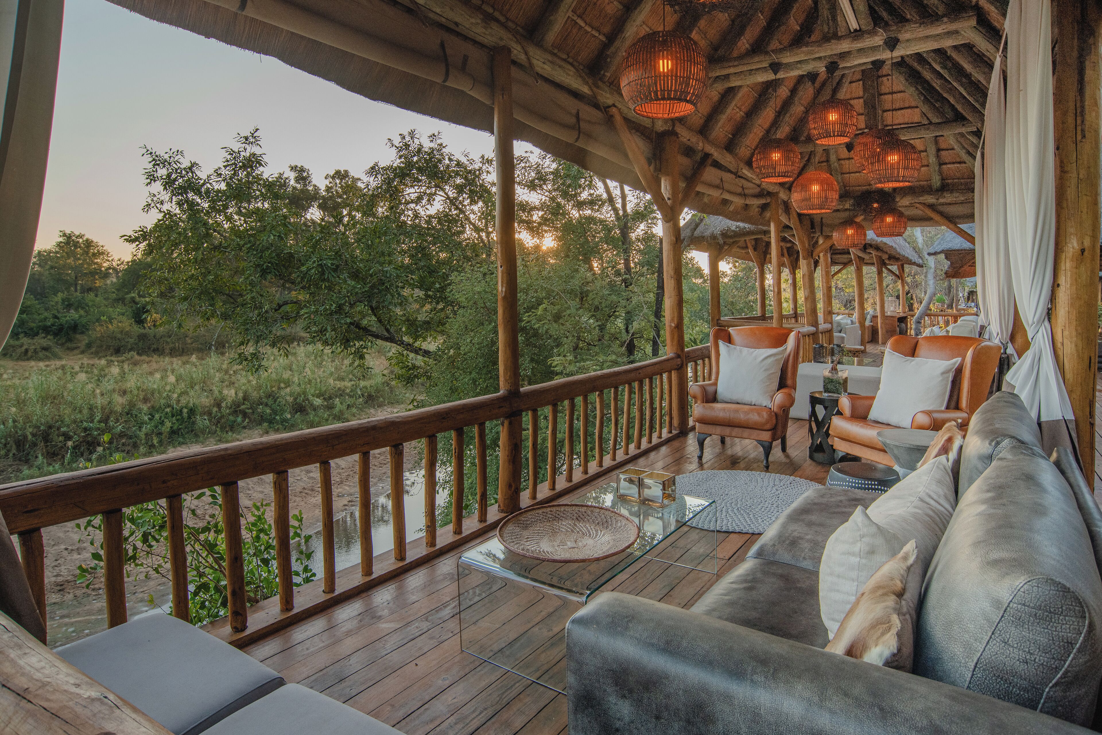 A wooden deck with a sofa and chairs, overlooking a natural landscape.