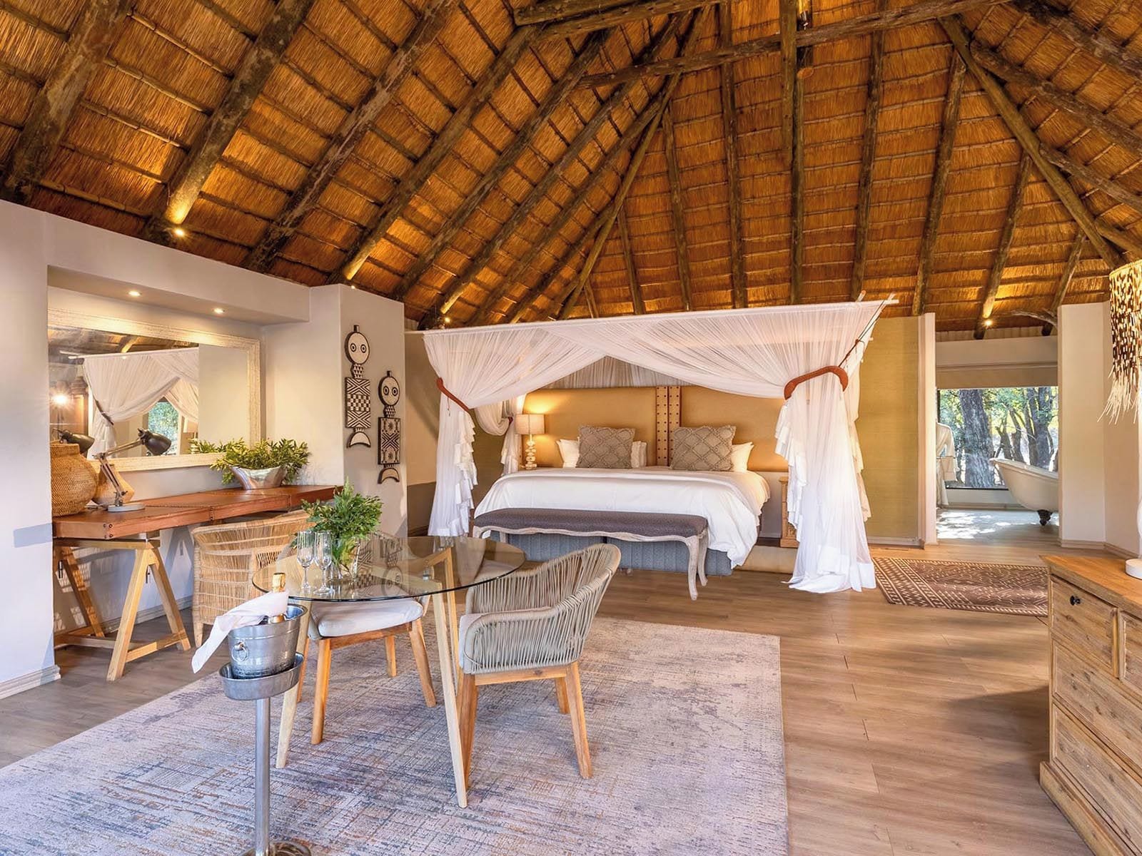 A bedroom with a canopy bed, a sitting area with a table and chairs, and a view of the outdoors.