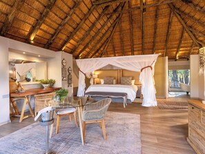 Un dormitorio con cama con dosel, una zona de estar con mesa y sillas, y vistas al exterior.