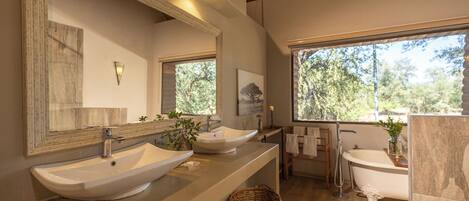 A modern bathroom with two sinks, a large mirror, and a bathtub.