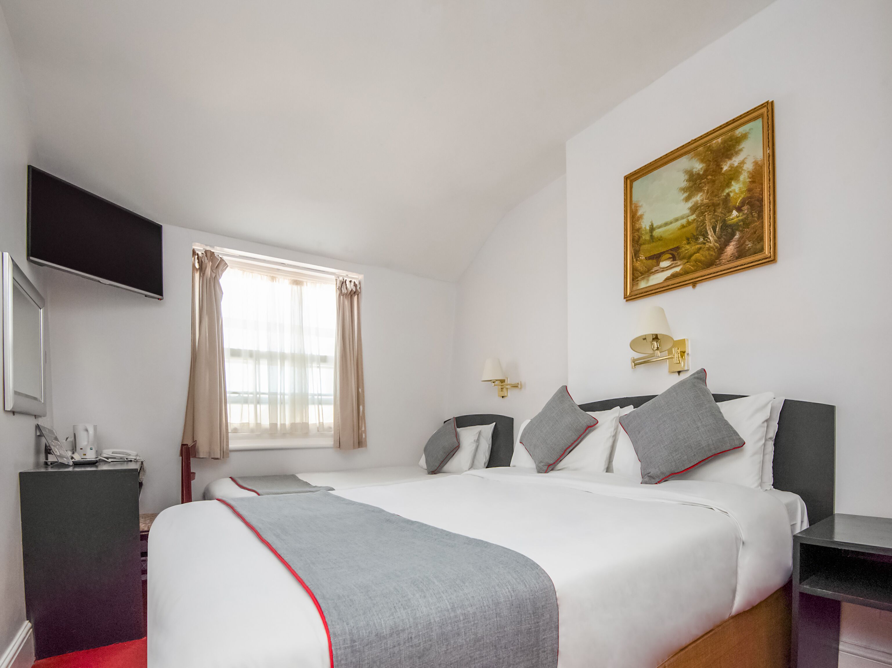 A hotel room with a large bed, a flat-screen TV, a desk, a lamp, and a painting on the wall.