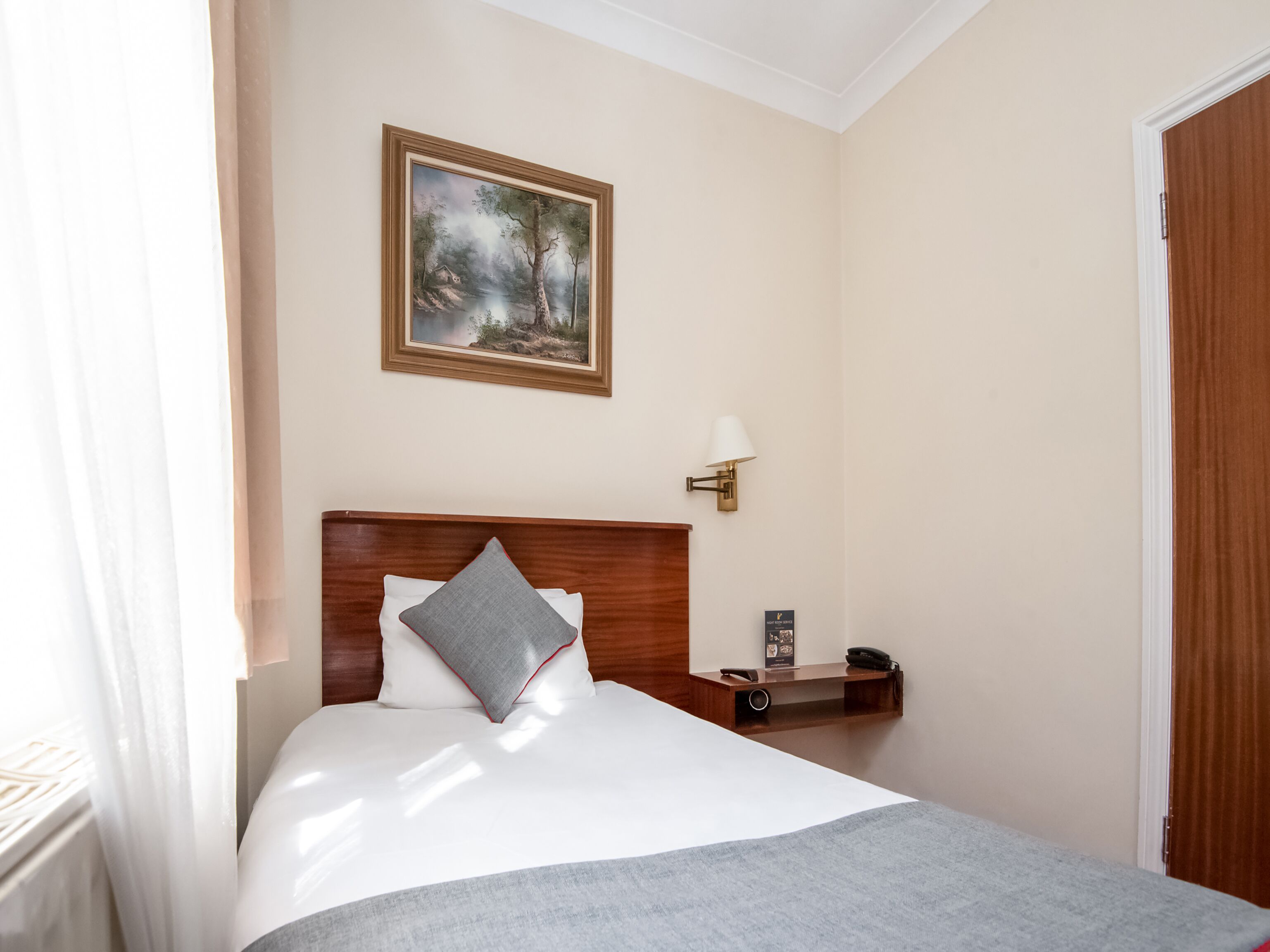 Une chambre d’hôtel avec un lit, une table de chevet, une lampe, un tableau et une porte.