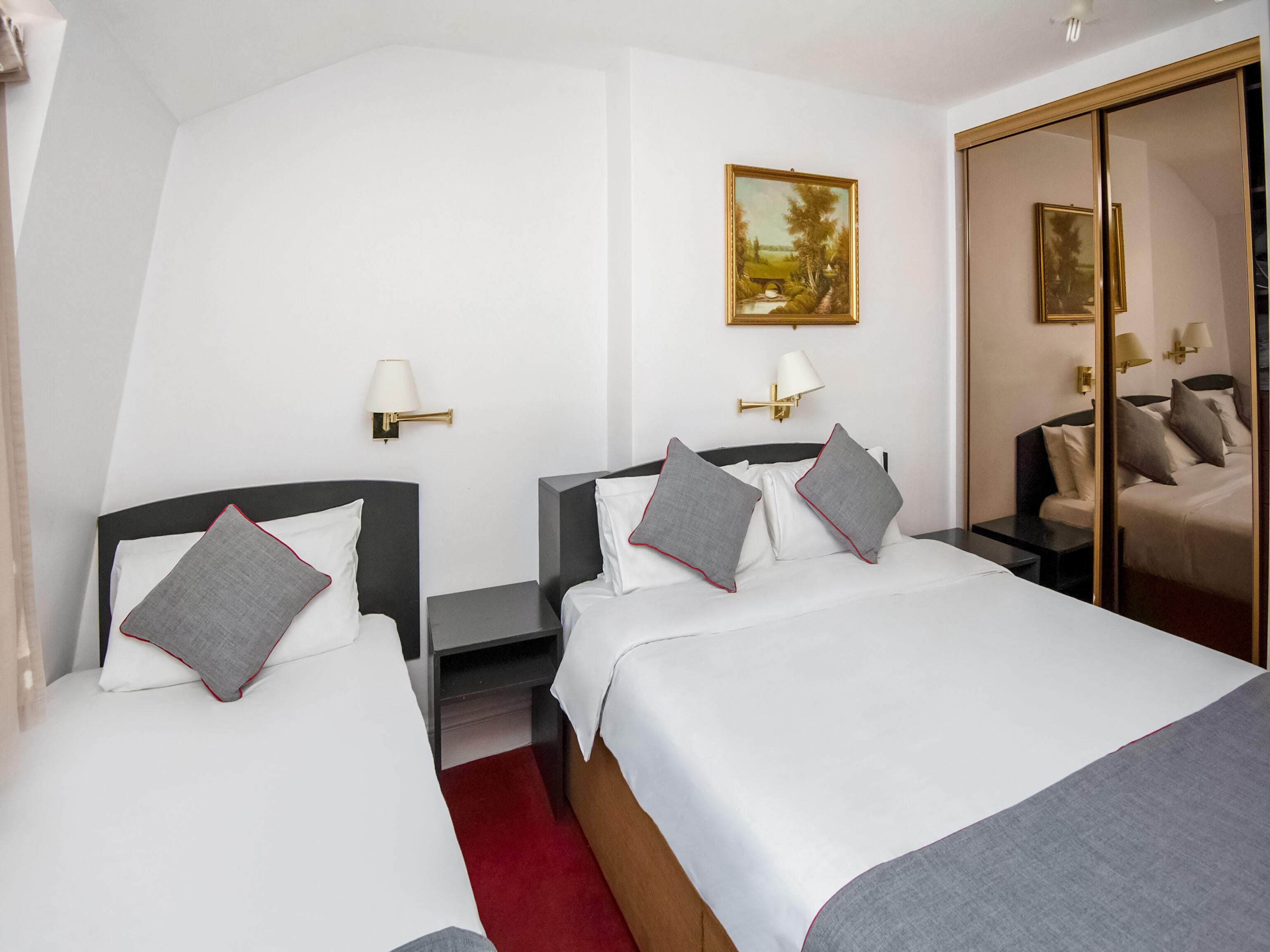 A hotel room with two beds, a red carpet, and a painting on the wall.
