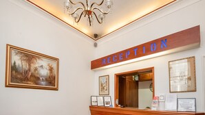 Un área de recepción con un mostrador de madera, un candelabro, obras de arte enmarcadas y un sofá gris con cojines rojos.