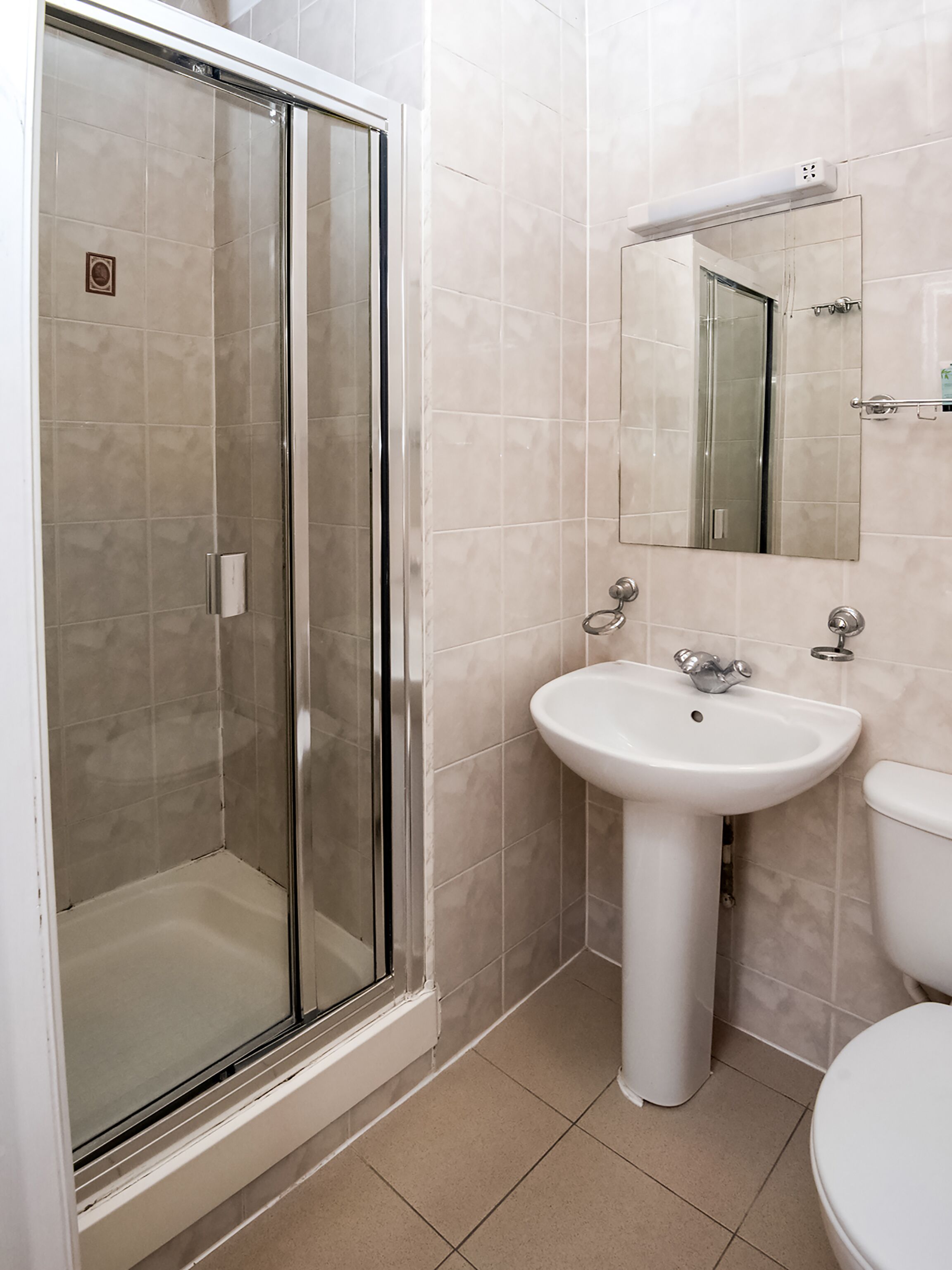 A bathroom with a glass-enclosed shower, a pedestal sink, and a toilet.