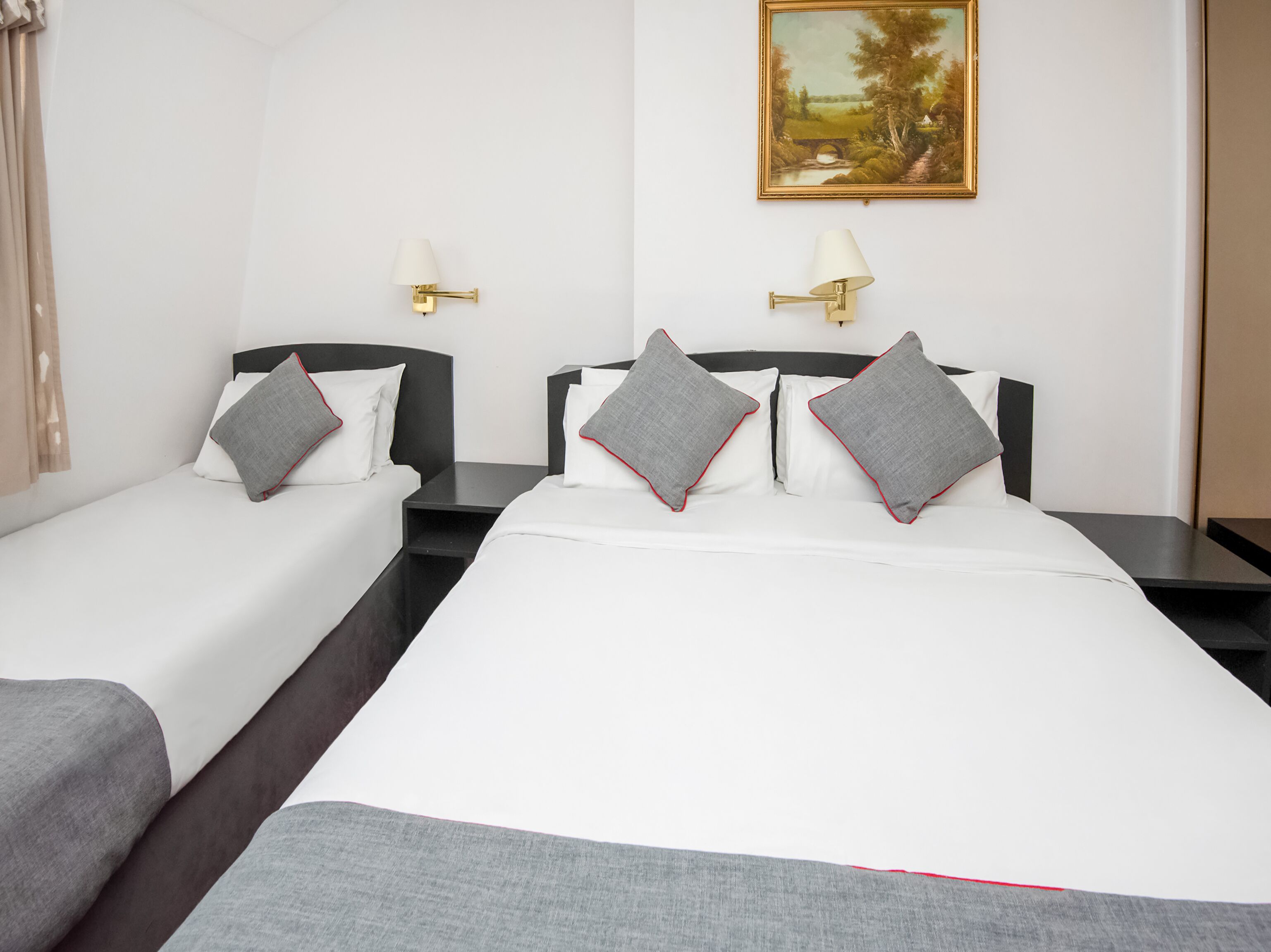 A hotel room with two single beds, a large bed, and a painting on the wall.