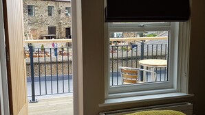 A room with a window overlooking a courtyard with outdoor furniture and a stone building in the background. - The Bowes Hotel (Hexham)