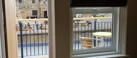 A room with a window overlooking a courtyard with outdoor furniture and a stone building in the background.