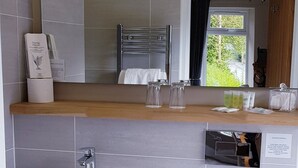 A bathroom with a sink, mirror, towel rack, and toiletries. - The Bowes Hotel (Hexham)
