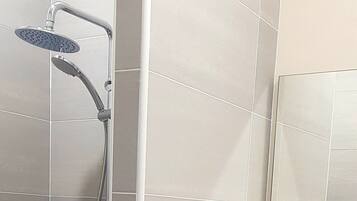 A shower with a handheld showerhead and a fixed overhead showerhead, mounted on a wall with large, light-colored tiles.