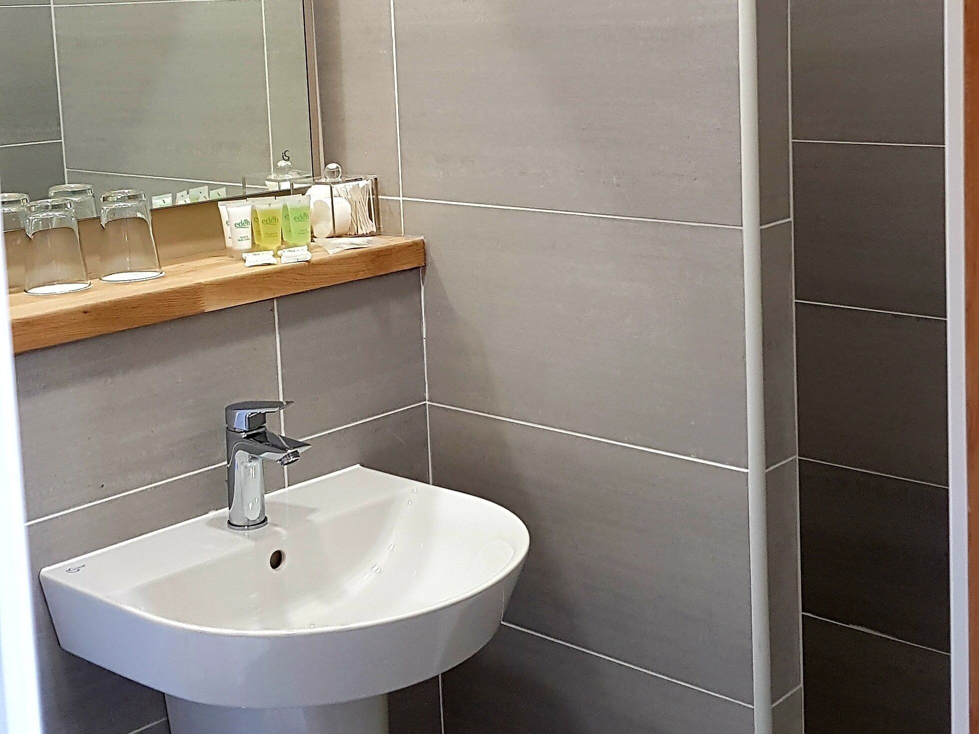 A bathroom with a white sink, a mirror, and a shelf with toiletries.