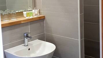 A bathroom with a white sink, a mirror, and a shelf with toiletries.