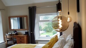 A bedroom with a bed, a bedside table, a mirror, a window, and a hanging light fixture. - The Bowes Hotel (Hexham)