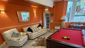 A room with a pool table, a sofa, a chair, and a fire exit sign. - Albemarle Hotel (Scarborough)