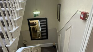 A staircase with white balusters and carpeted steps leading to a landing with a light fixture and a framed picture. - Albemarle Hotel (Scarborough)