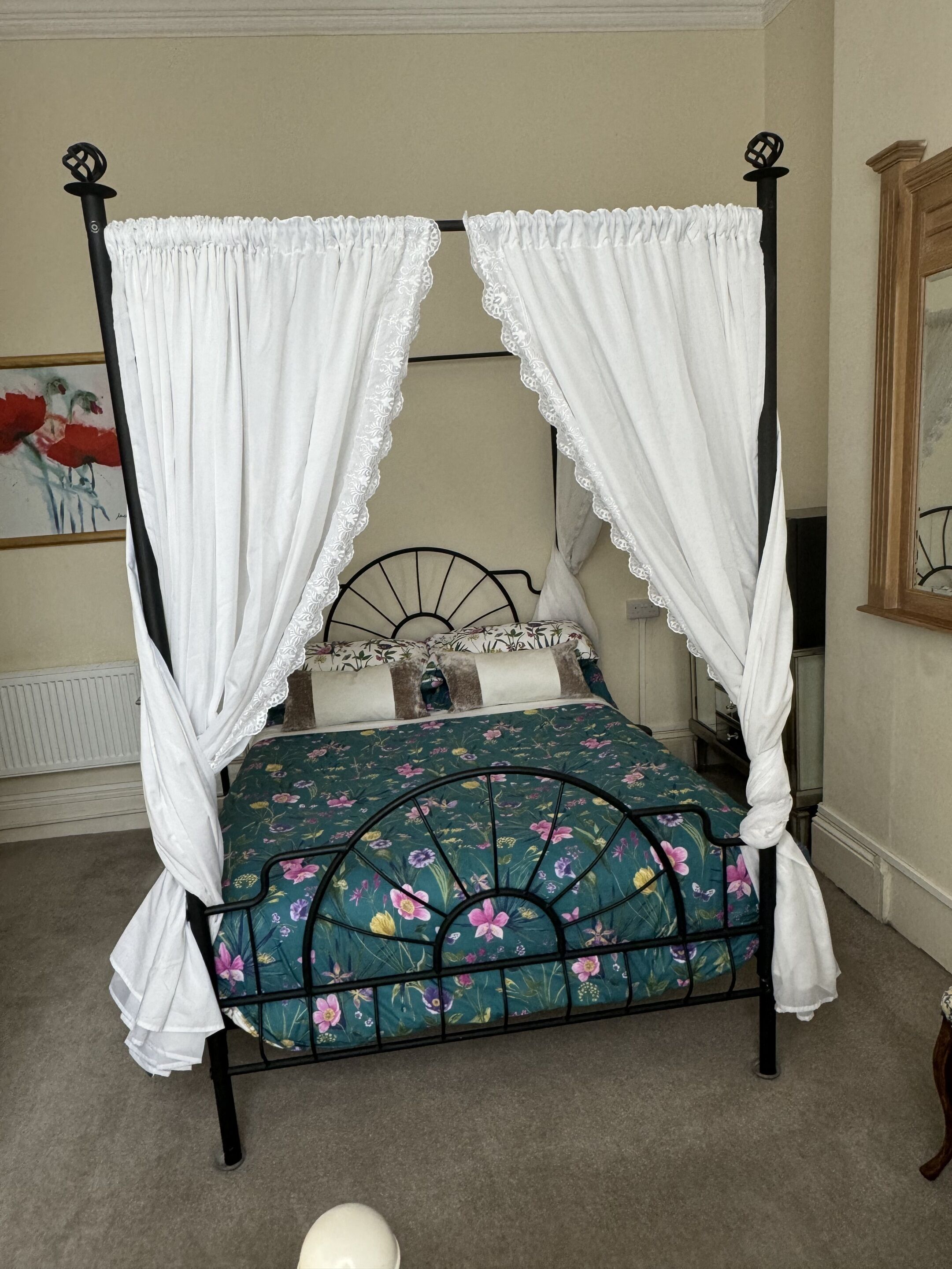 Un lit à baldaquin avec une couvre-lit à motifs floraux, des rideaux blancs et un haut-parleur fixé au mur.