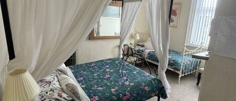 A four-poster canopy bed with floral bedding, a bedside table with a lamp, and a small cabinet.
