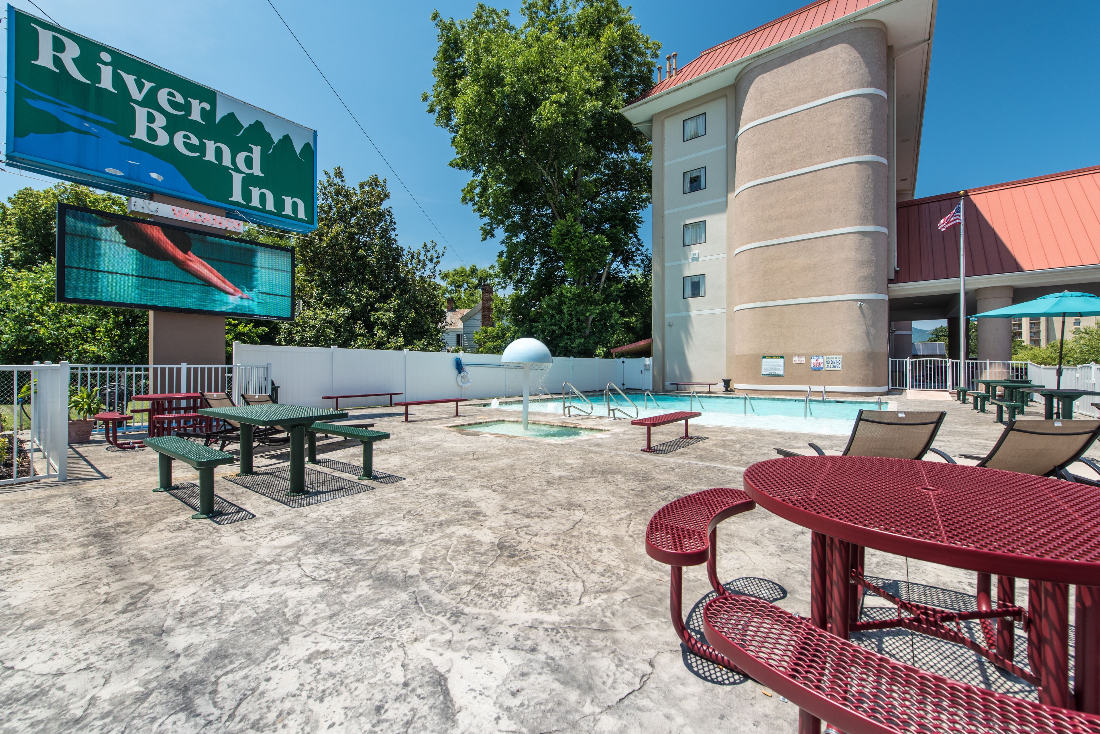 A pool area with picnic tables and lounge chairs, a large sign for River Bend Inn, and a building with a red roof.