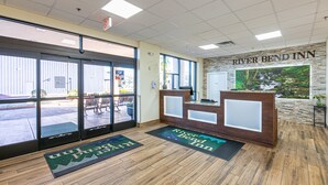A hotel reception area with a wooden reception desk, a large window, and a welcome mat. - River Bend Inn (Pigeon Forge)