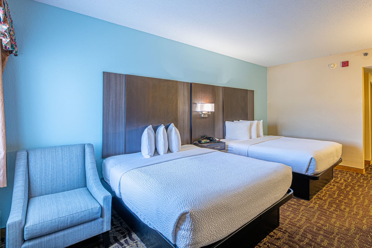 A hotel room with two beds, a chair, a nightstand, and a lamp.