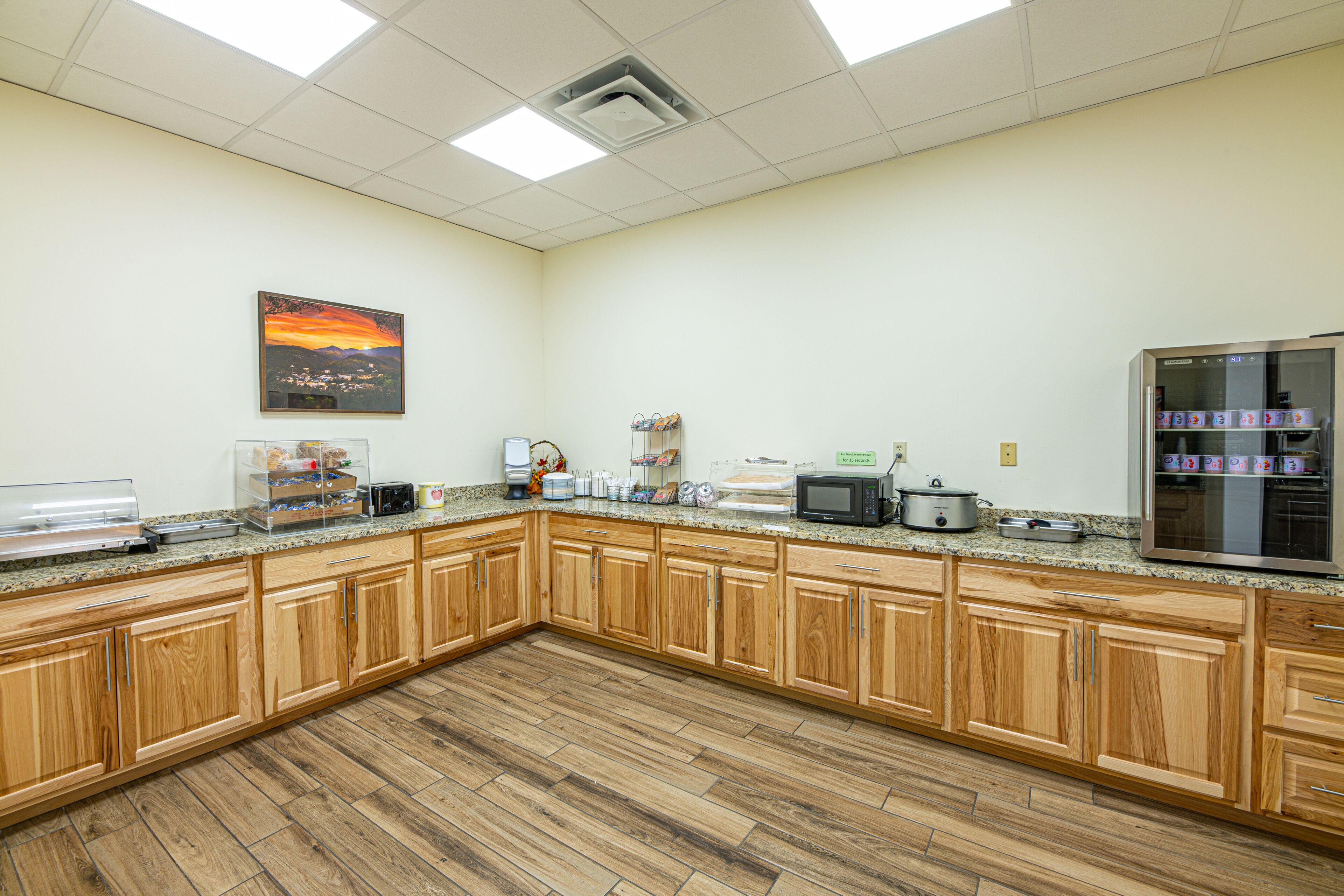 A kitchen with wooden cabinets, granite countertops, a microwave, a refrigerator, and a painting on the wall.